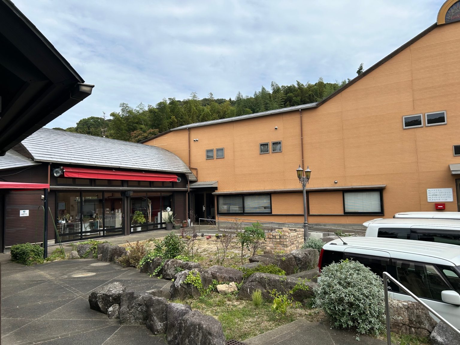 介護施設の外観。オレンジ色のレンガ造りの建物で、玄関部分と駐車スペースが見える。
