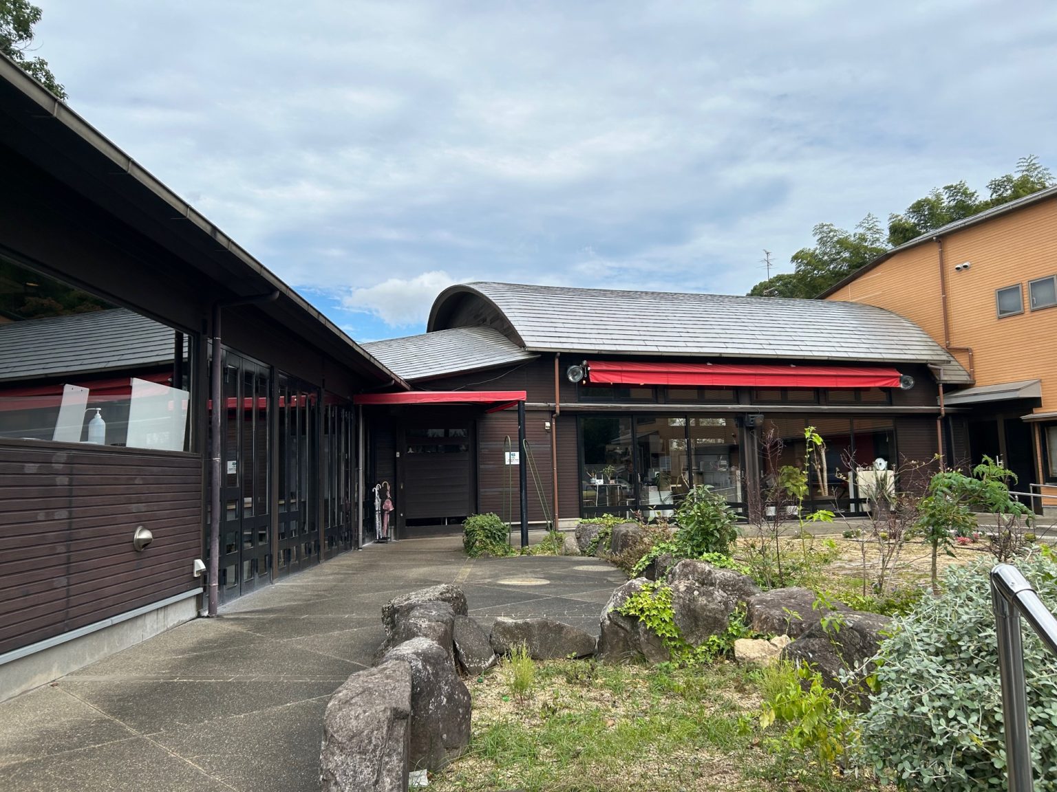 介護施設の建物外観。モダンデザインの黒と赤の外壁、広い庭園エリア